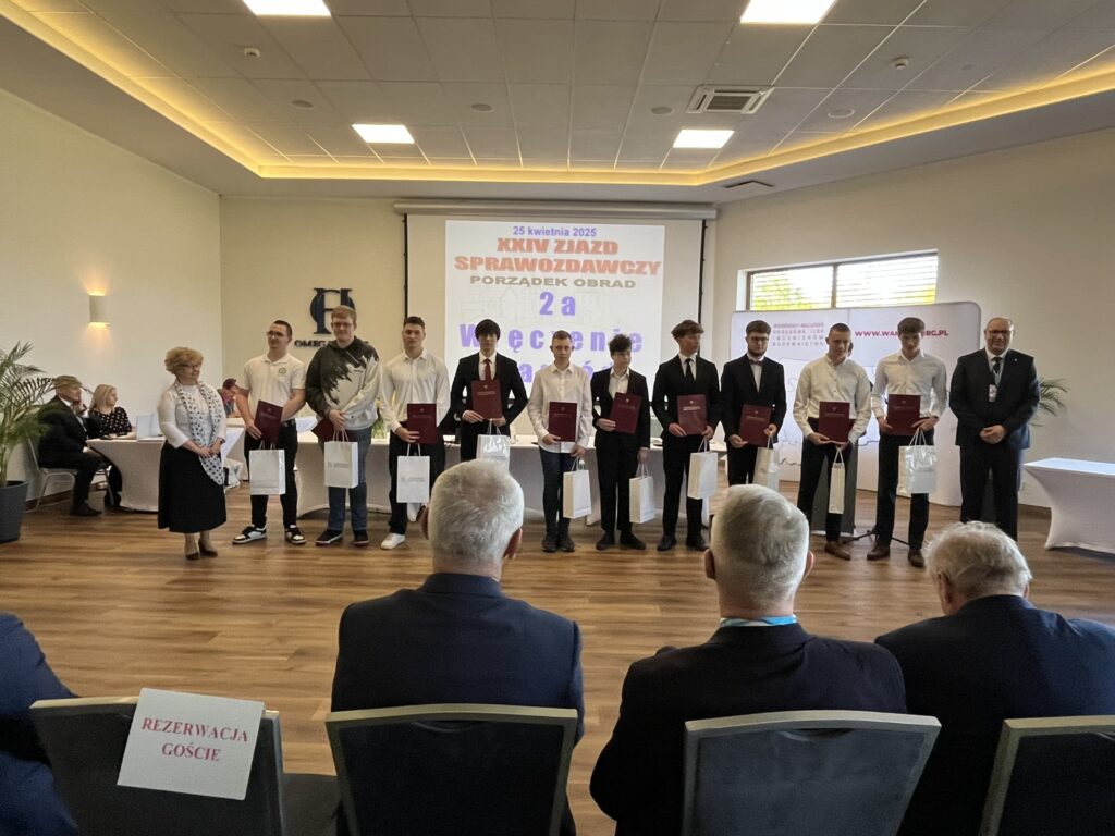 Na zdjęciu grupa uczniów techników budownlanych z woj Warmińsko Mazurskiego stoi na scenie podczas uroczystości, trzymając dyplomy i upominki.