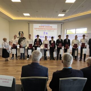 Na zdjęciu grupa uczniów techników budownlanych z woj Warmińsko Mazurskiego stoi na scenie podczas uroczystości, trzymając dyplomy i upominki.