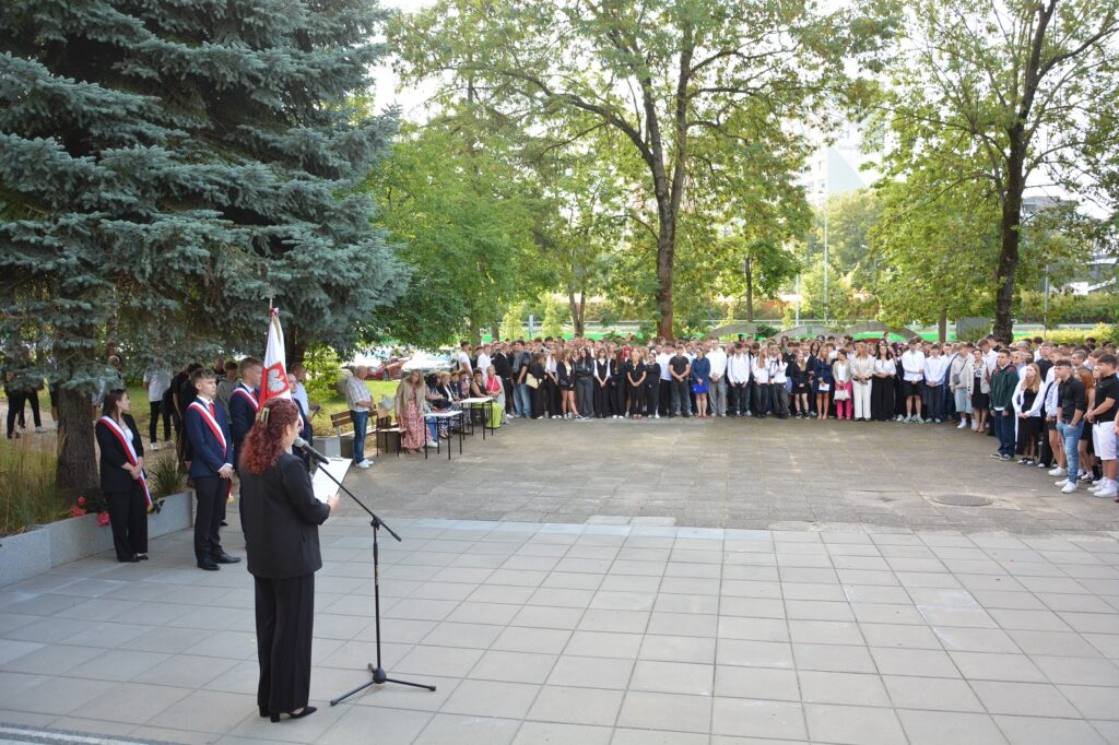 uroczyste rozpoczecieroku szkolnego zdjęcie grupowe na placu przed szkola
prowwadzaca